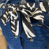 Blue jeans door stop with a zebra-patterned belt on a wooden floor.