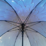 A close-up view from underneath of a large flower-print umbrella, showing pale blue and white petal-like panels radiating from a black central hub and pole.