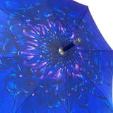 A close-up of a vibrant royal blue umbrella with a large, detailed floral mandala pattern in shades of blue and purple, featuring a dark handle and gold accents.