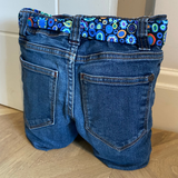 Blue jeans door stop with a colorful belt on a wooden floor.