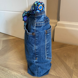 Blue denim door stop with a patterned belt on a wooden floor.
