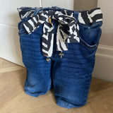 Blue jeans door stop with a patterned tie on a wooden floor against a white wall.