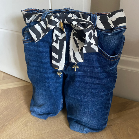 Blue jeans door stop with a patterned tie on a wooden floor against a white wall.