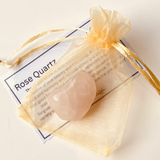 Rose Quartz crystal in a clear bag with gold drawstring on a white background
