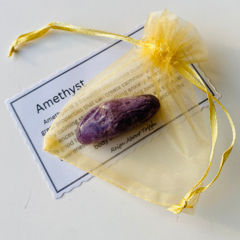 Purple amethyst crystal in a yellow drawstring bag with an information card on a white background