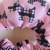 Pink scrunchie with black plaid dog pattern on a light pink background