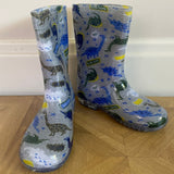Pair of children's rain boots with dinosaur pattern on a wooden floor.