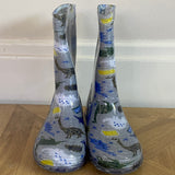 Pair of children's rain boots with dinosaur design on a wooden floor.