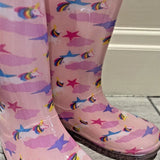 Pink rain boots with unicorn and rainbow patterns on a light gray floor.